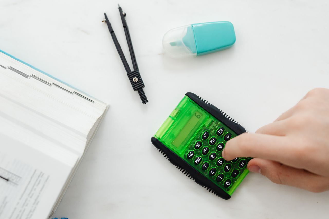service-03 Close-up of a hand using a green calculator with stationery for studies or business calculations.